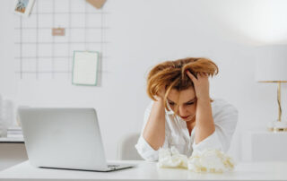 woman at desk with laptop with her head in hands
